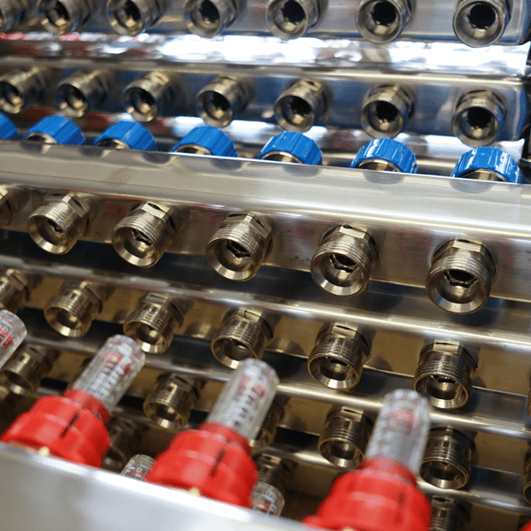 Close-up of several stainless steel manifolds with red flow meters and blue plastic caps.
