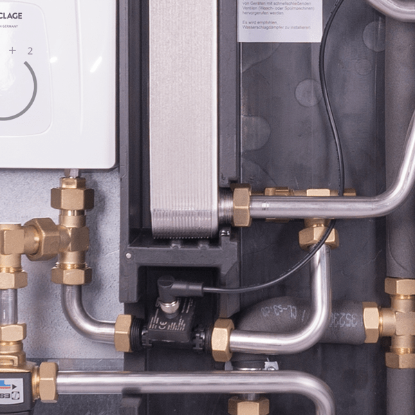 Close-up of a home station with metal pipes, a stainless steel plate heat exchanger and a white reheater.