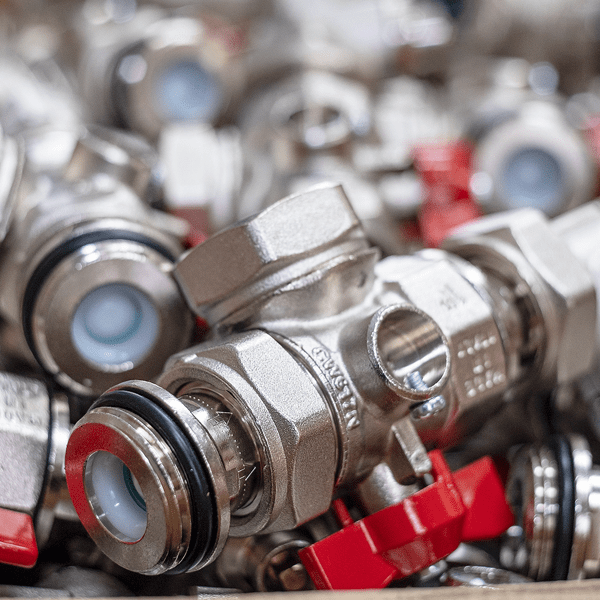 Nahaufnahme mehrerer verchromter Metallventile mit roten Griffen und Dichtungen.